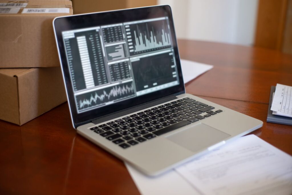 pexels photo 7857560 7857560 Laptop showing data graphs on wooden table with cardboard boxes, depicting a small business office setting.